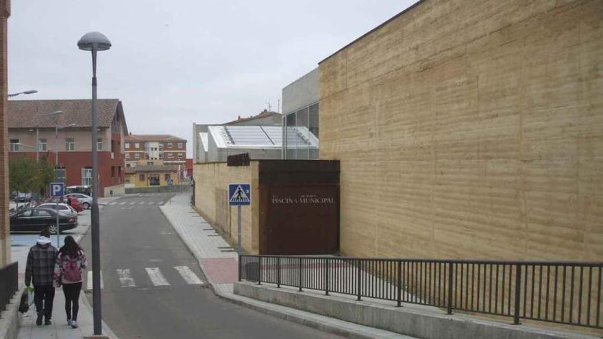 Dos vecinos pasean junto al recinto en el que se encuentra el servicio de la piscina climatizada. Foto