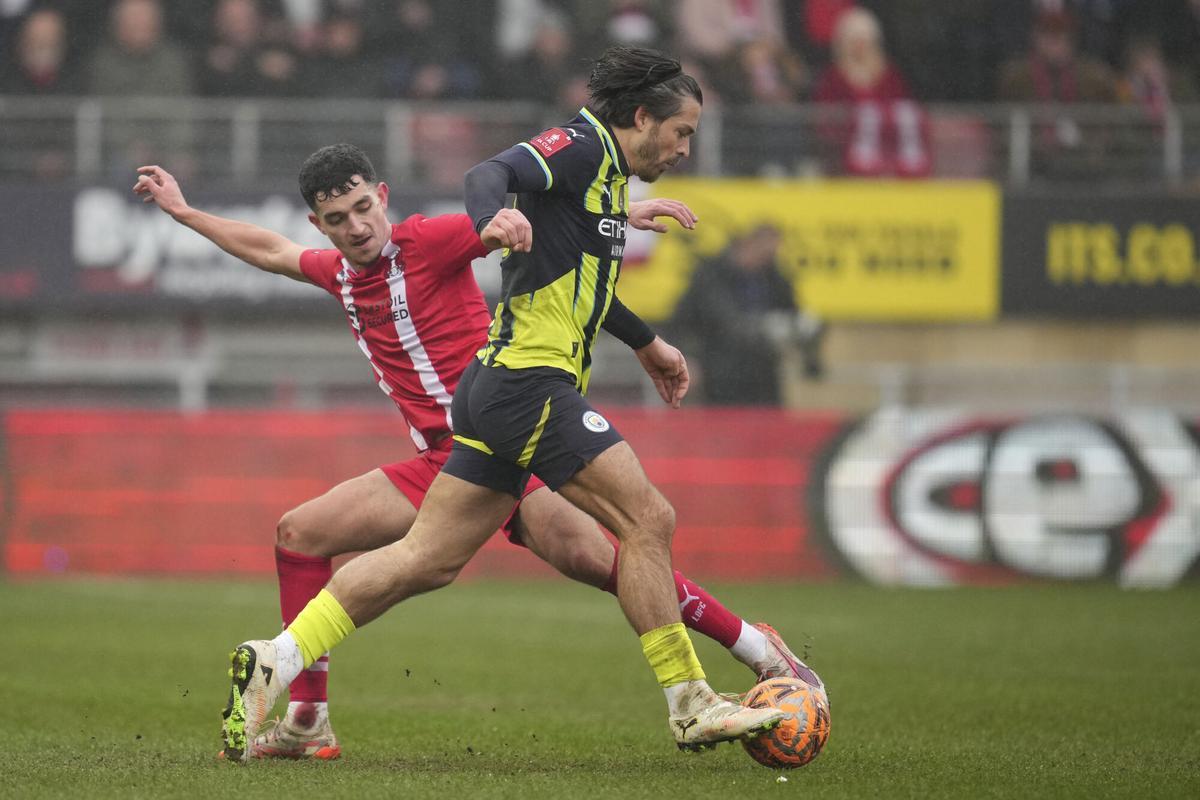 Manchester City's Jack Grealish, right, challenges for the ball with Leyton Orient's Sonny Perkins during the English FA Cup fourth round soccer match between Leyton Orient and Manchester City at the Gaughan Group Stadium in London, England, Saturday, Feb. 8, 2025. (AP Photo/Kin Cheung)