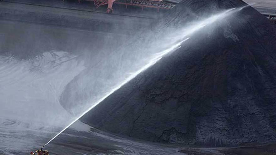 Un aspersor lanza agua sobre una parva de carbón en El Musel. autoridad portuaria de gijón