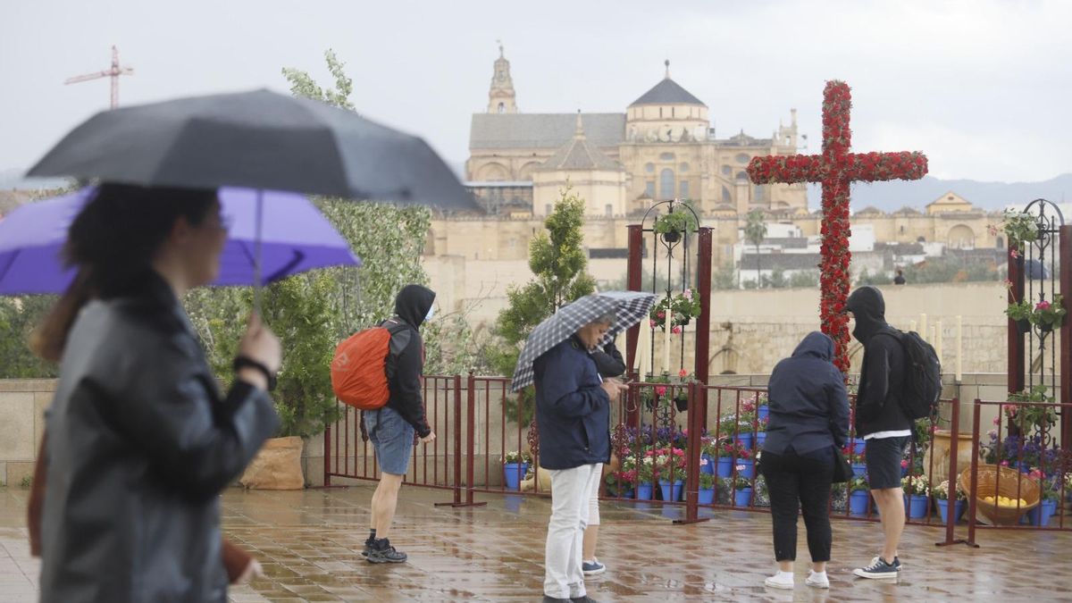 Turistas visitan una cruz de mayo bajo la lluvia en Córdoba.