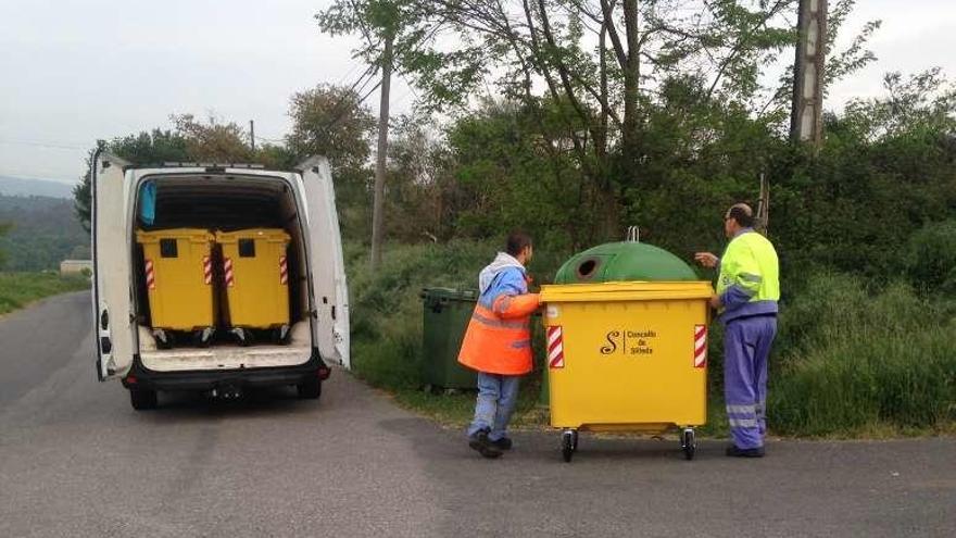 Dos operarios colocan contenedores amarillos en una parroquia.