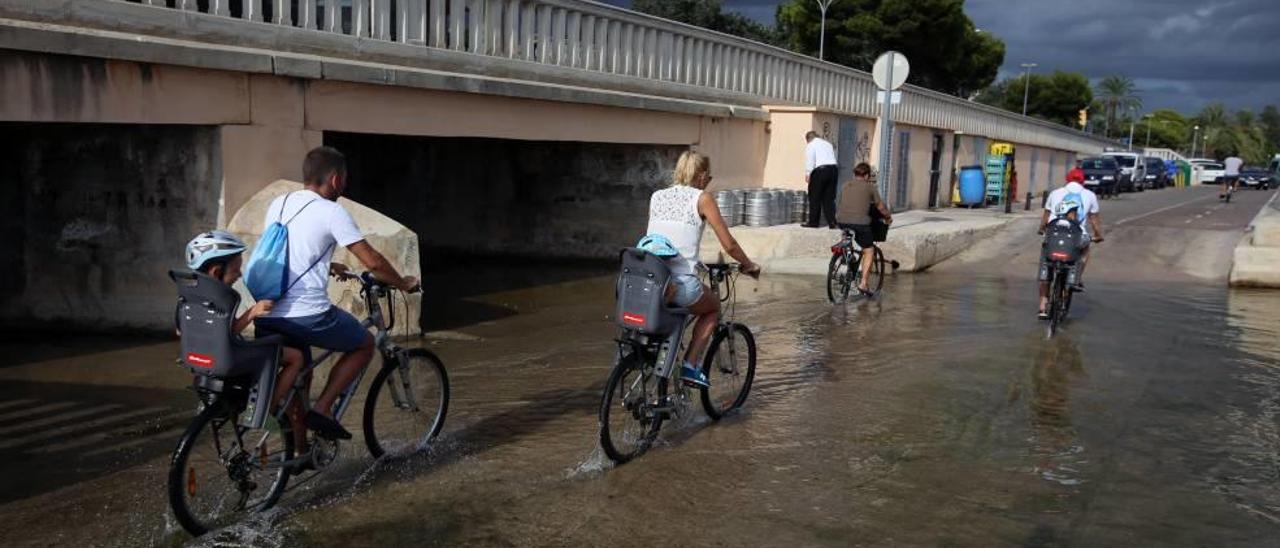 Turistas atravesando el carril bici anegado por el agua del mar.