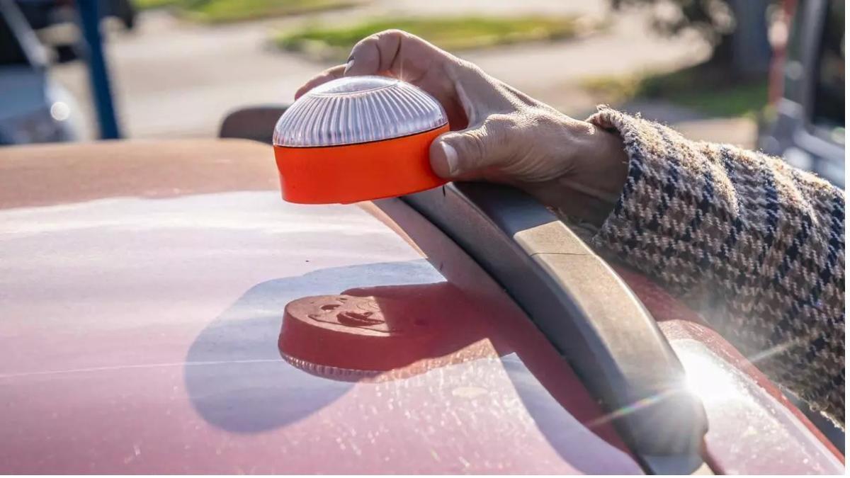 Una mujer coloca una baliza V16 en el capó de su coche.