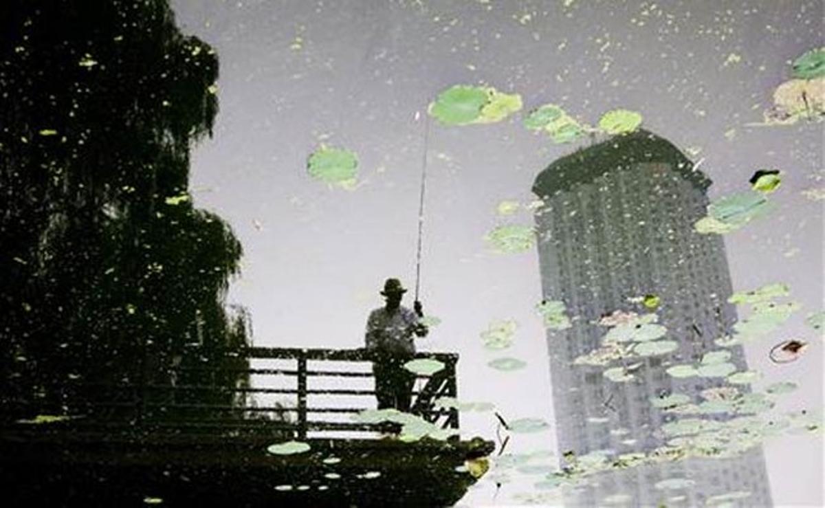 Reflex a l’aigua d’un home pescant en un canal a Pequín (Xina).