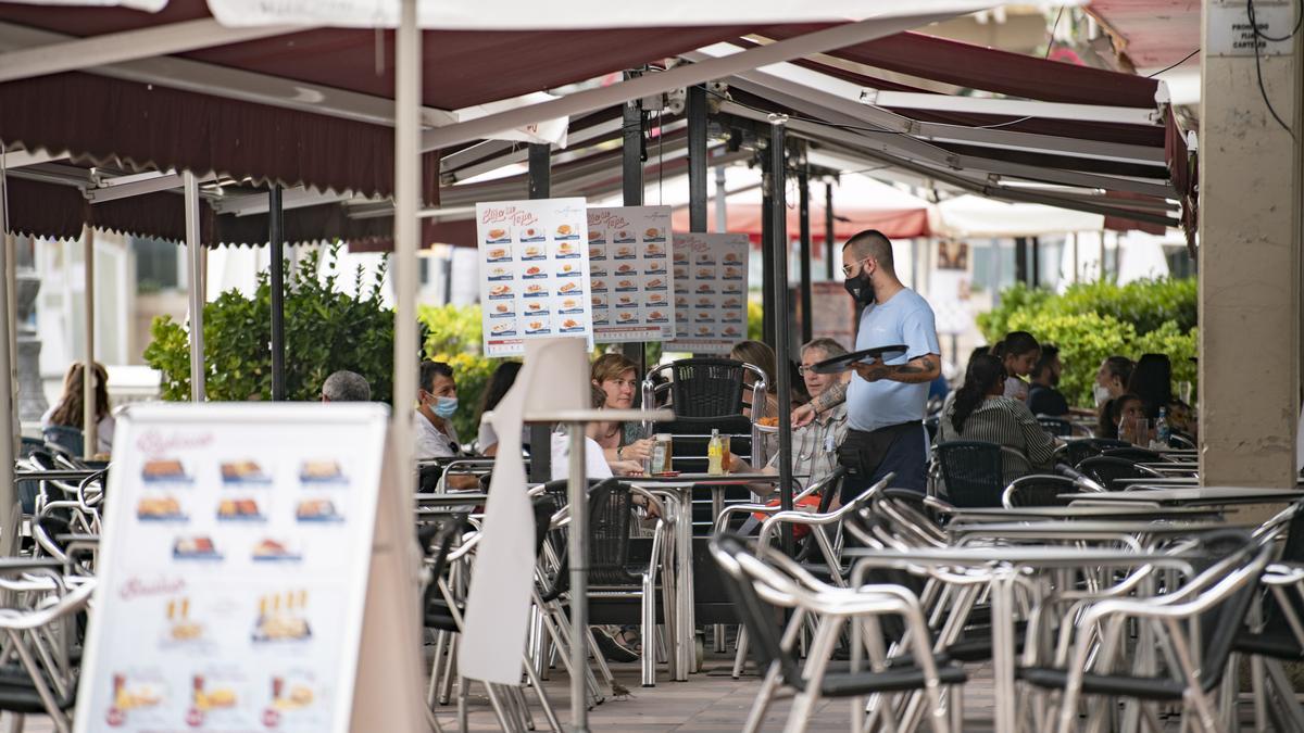 Un camarero atiende una mesa en la terraza de una cafetería.