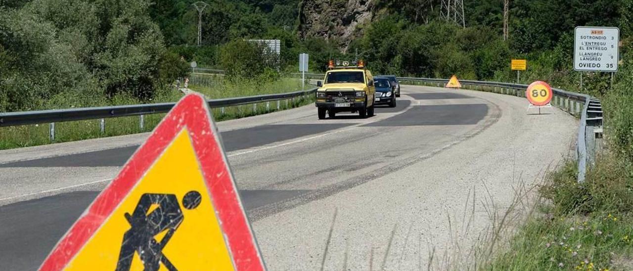 Vehículos circulando por el Corredor en la zona entre Barredos y Blimea, con partes del firme rebacheadas y abundante gravilla en la plataforma de la carretera.