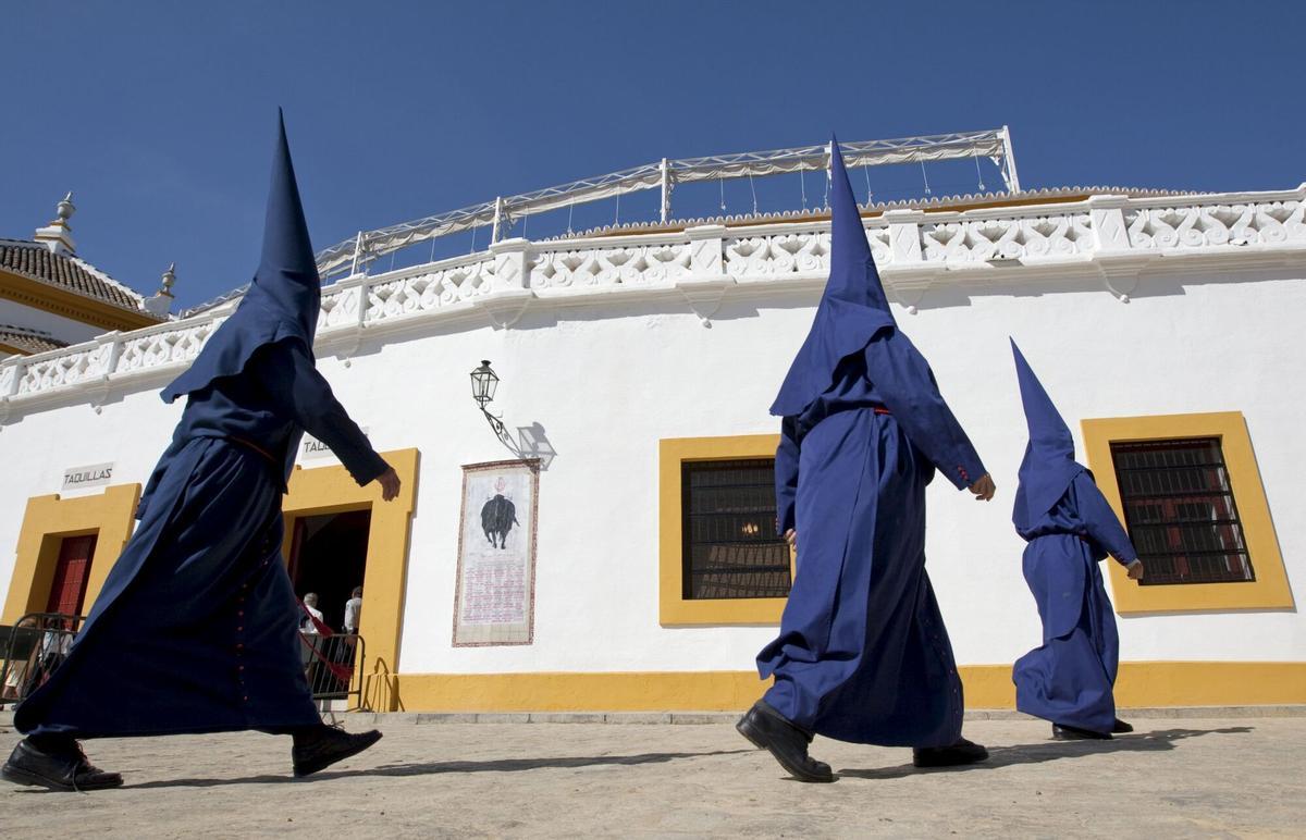 Nazarenos de la Hermandad del Baratillo pasan junto a la Real Maestranza de Sevilla, camino de la capilla de la Piedad para iniciar su estación de penitencia