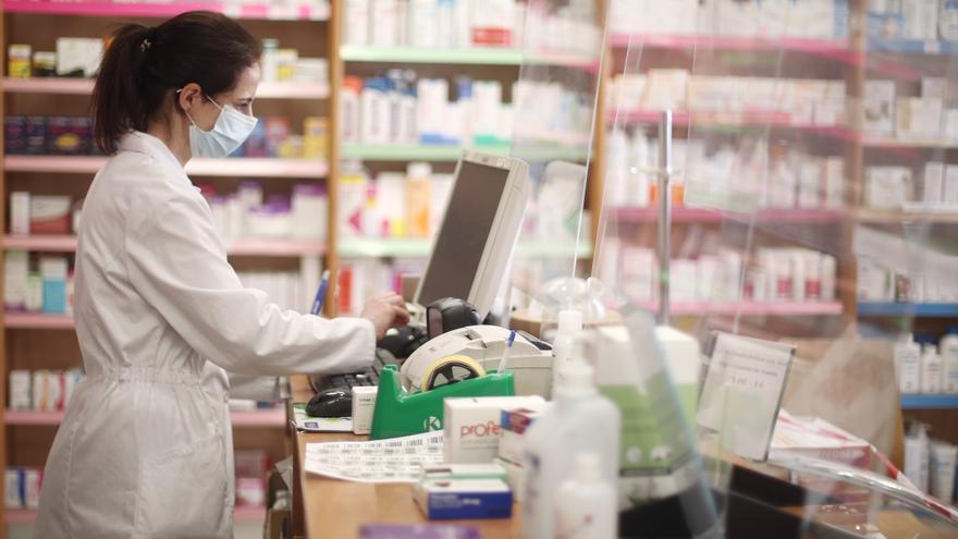 Una farmacéutica con mascarilla despacha en una farmacia.