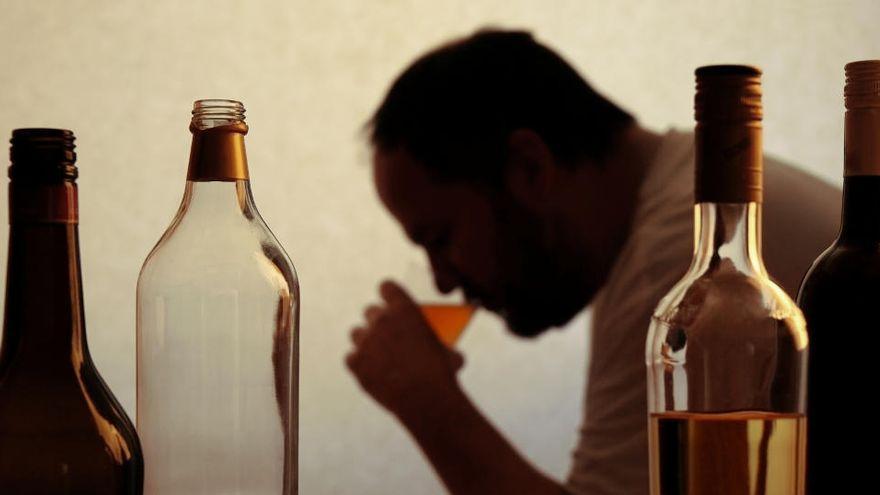 Un hombre toma un trago, rodeado de botellas.