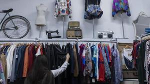 Una mujer mira ropa vintage de segunda mano en la tienda La Vespa Roja, de València.