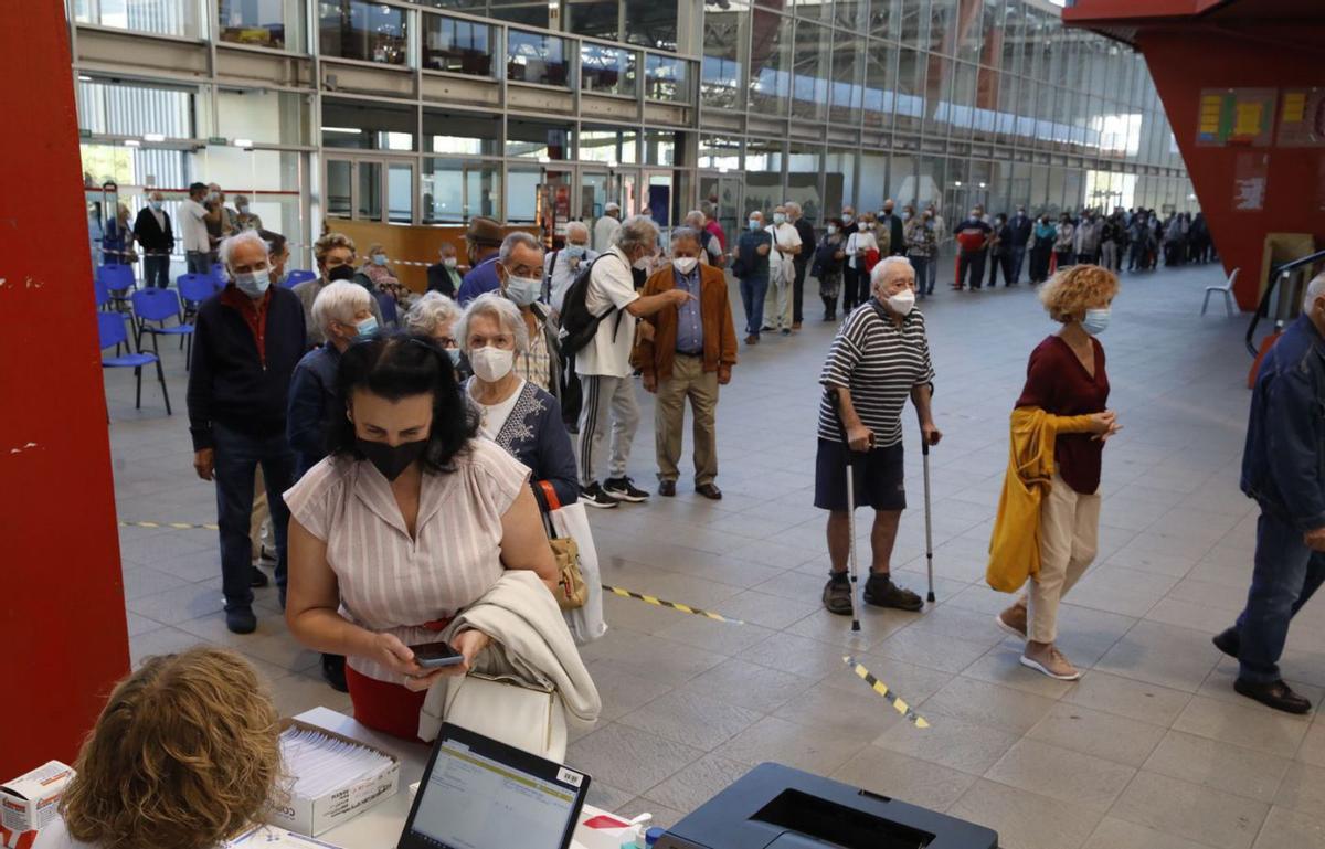 En la imagen superior, colas en el nuevo punto de vacunación del mercado de Pola de Siero. Sobre estas líneas, pacientes esperando en el Palacio de Deportes de La Guía (Gijón). | Luján Palacios / Ángel González
