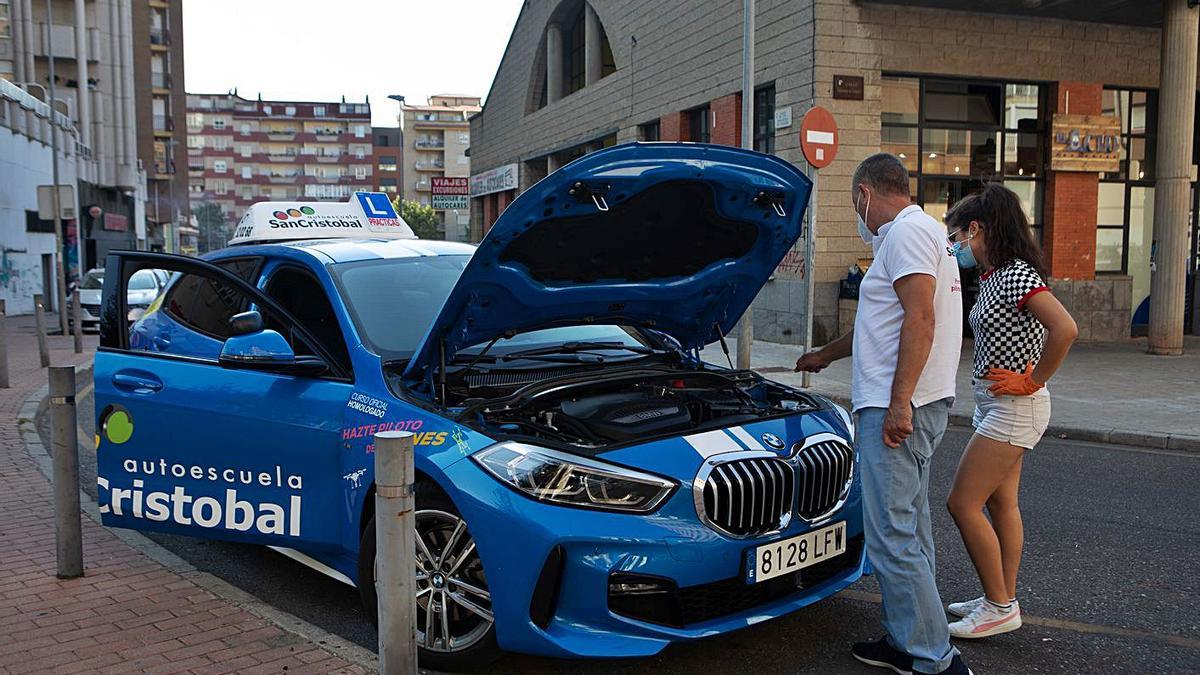 Un profesor de autoescuela revisa el coche junto a una alumna.