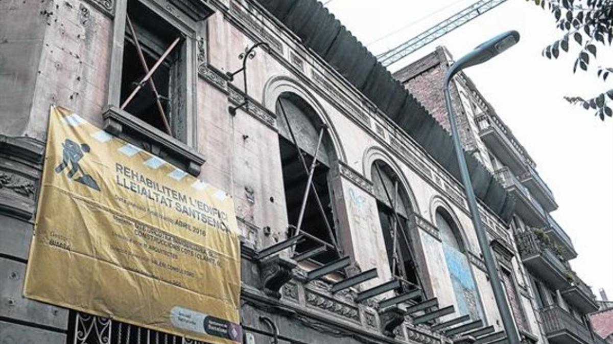 Fachada principal del edificio de La Lleialtat Santsenca, con las ventanas apuntaladas y con un cartel con los datos de las empresas que no acabaron la rehabilitación.