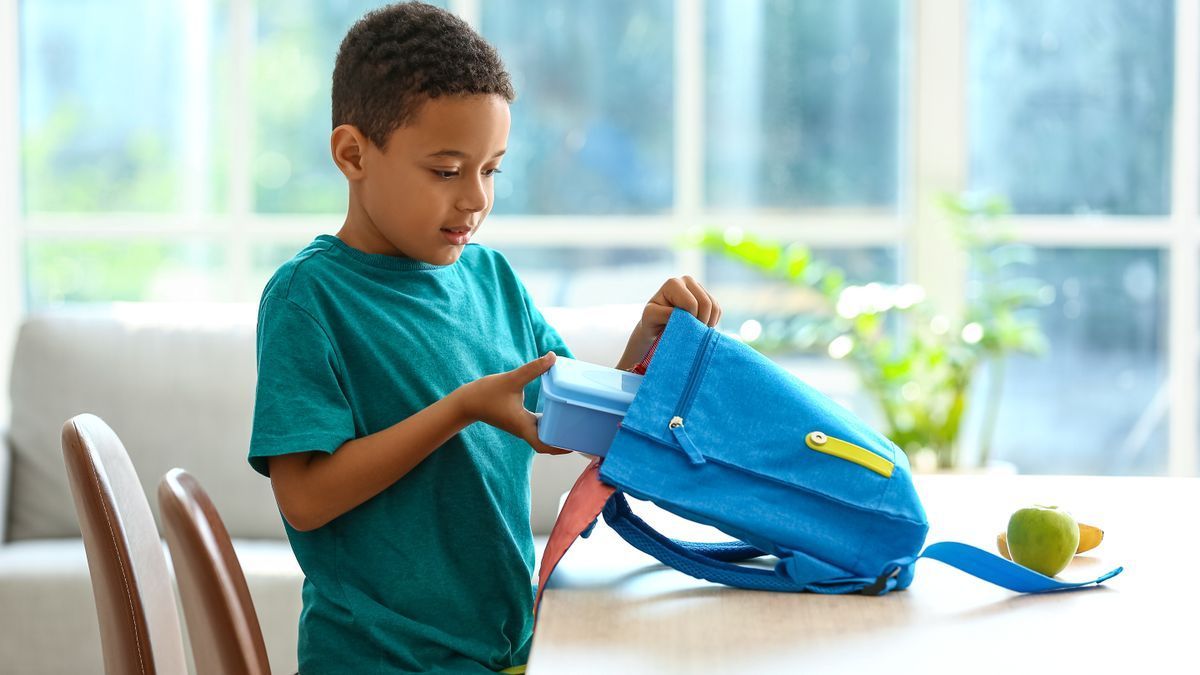 Un niño guarda el tupper con su almuerzo en su mochila.