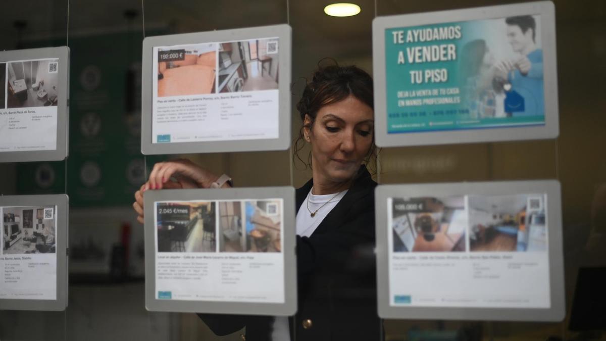 Una trabajadora cuelga un cartel de un piso en venta en una inmobiliaria de Zaragoza.