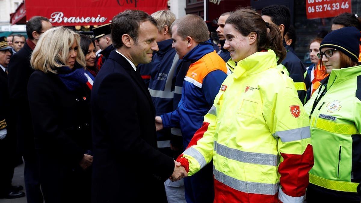 Macron y su mujer, Brigitte (izq), saludan a miembros de los servicios de emergencia delante del bar Comptoir Voltaire, durante una ceremonia por el segundo aniversario de los atentados de París, el 13 de noviembre.