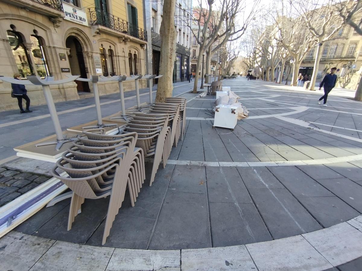 Cadires i para-sols d'una de les terrasses, ben plegades davant d'un Passeig buit