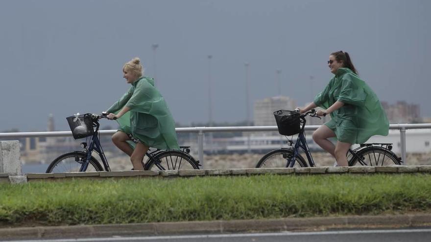 Dos turistas montan en bici con chubasqueros para cubrirse de las lluvias en Palma.