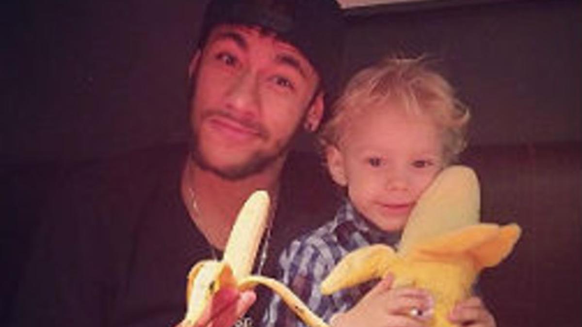 Neymar se come un plátano junto a su hijo, que sostiene un plátano de peluche.