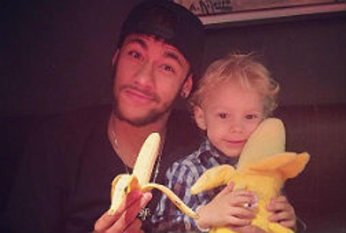Neymar es menja un plàtan al costat del seu fill, que sosté un plàtan de peluix.