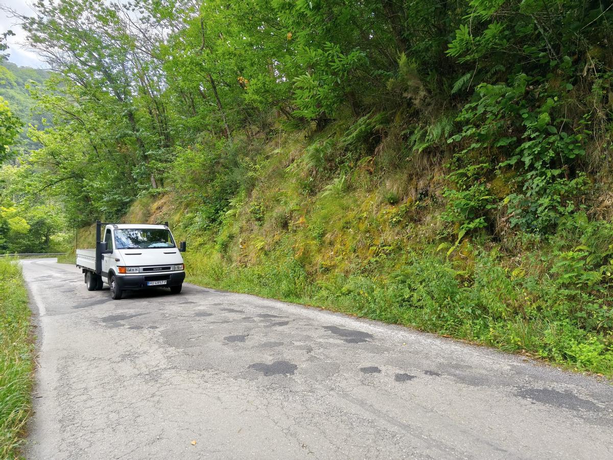 Una camioneta de trabajo pasa por una zona de baches en la AS-311 entre San Pedro de los Burros y Cubia, en Grado.