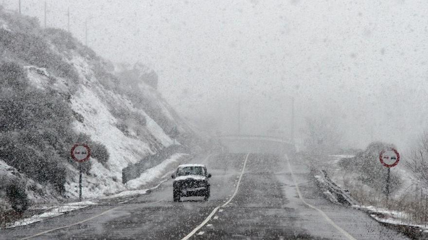 Un coche circula por una carretera nevada.