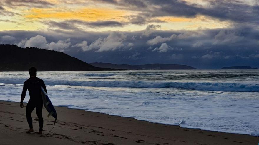 Un surfista pasea por el litoral de la playa de Razo / turismo de carballo