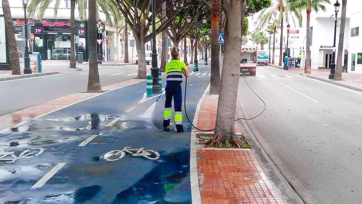 Una operaria de Limpieza baldea uno de los carriles bici que transitan por Puerto Banús.