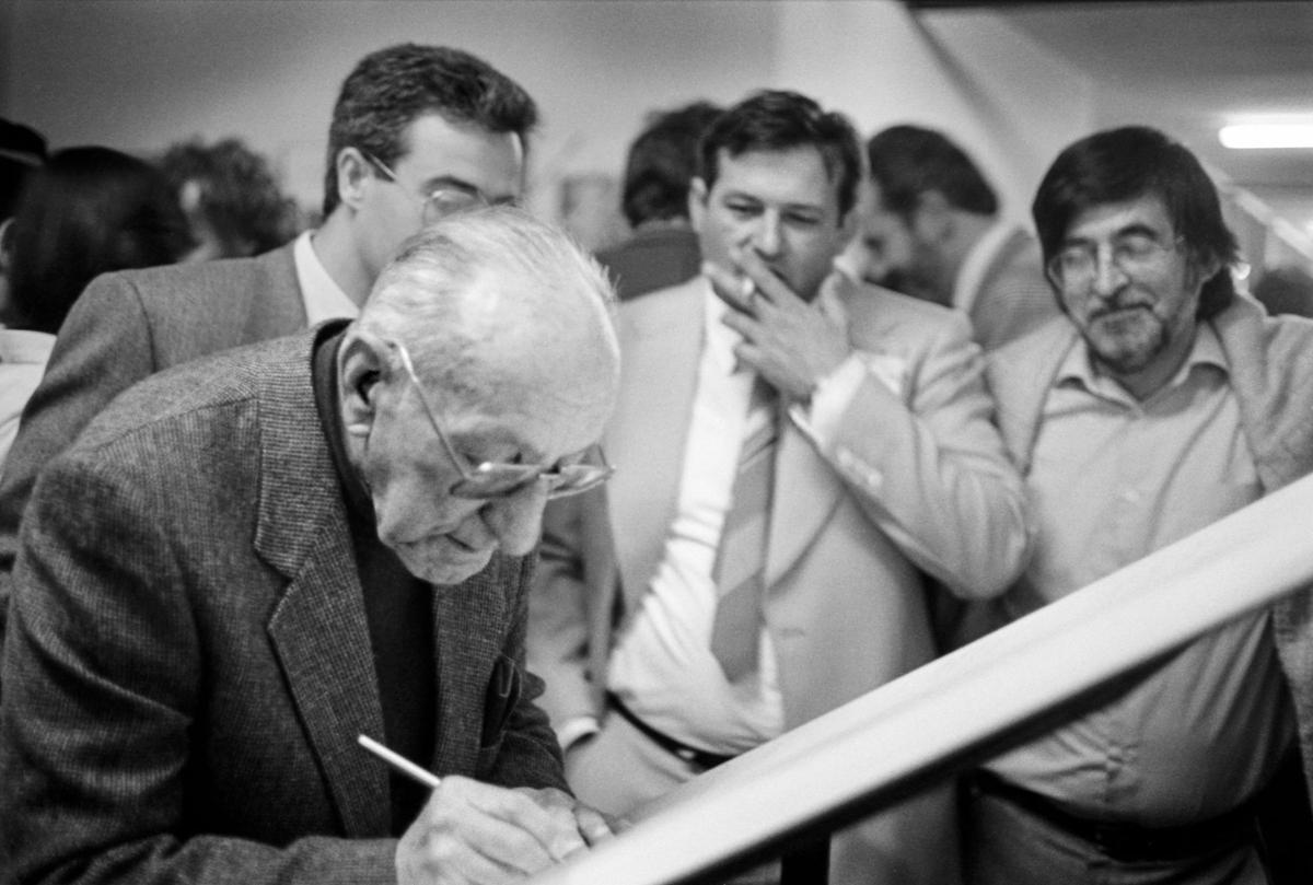 El mestre Enric Soler i Godes signant al llibre de les I Trobades d'Escola Valenciana, en abril de 1986 al CEIP Trullàs de Benifaió, davant la mirada de Josep Chaqués i Honorat Ros.