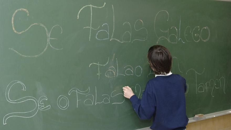 Un alumno escribe en galego na pizarra da clase.