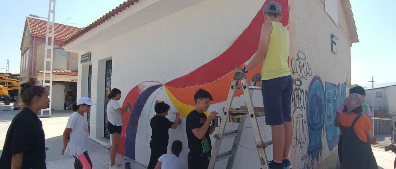 Los niños pintan un mural en uno de los edificios de la estación de Chapela.