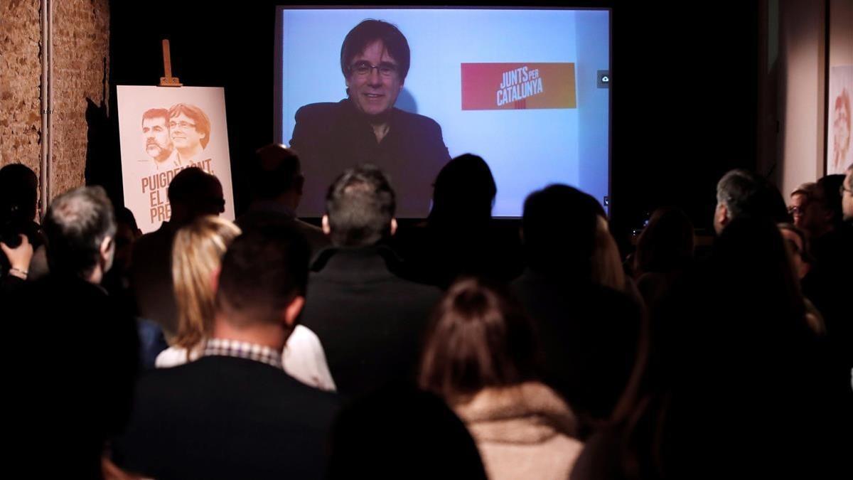 Carles Puigdemont conversa por videoconferencia con candidatos y simpatizantes durante la inauguración de la sede de campaña de Junts per Catalunya.