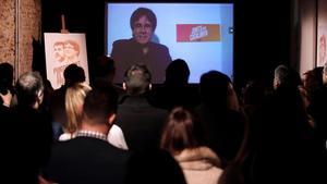 Carles Puigdemont conversa por videoconferencia con candidatos y simpatizantes durante la inauguración de la sede de campaña de Junts per Catalunya.