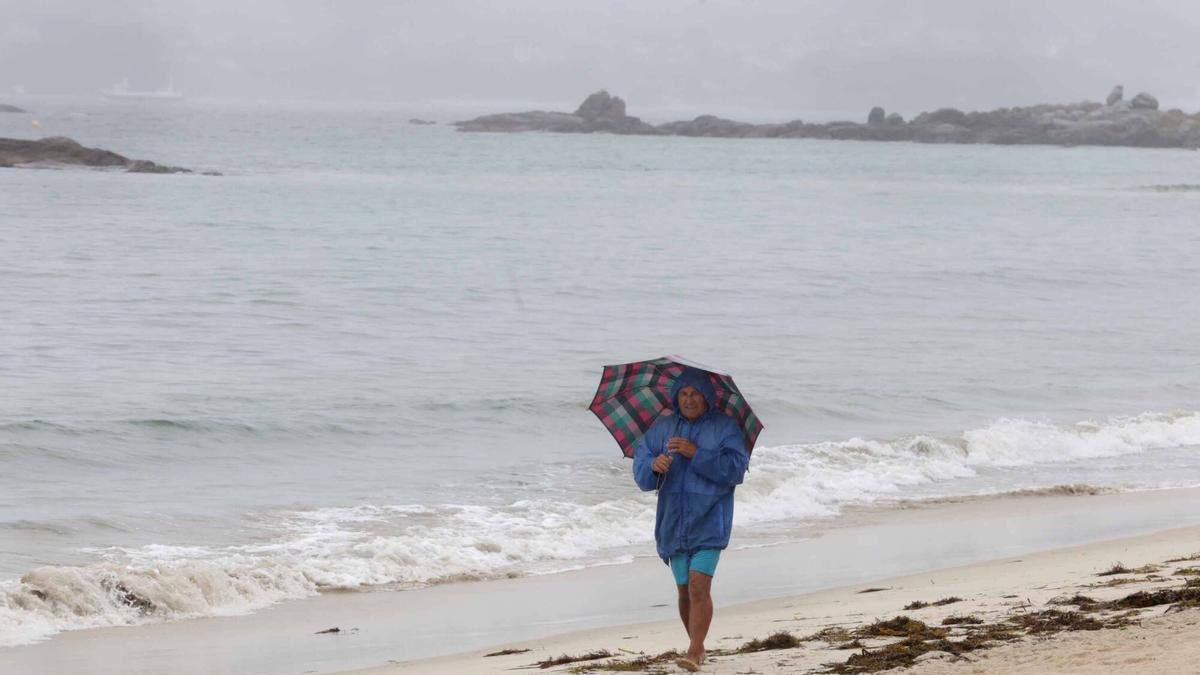 Una persona bajo la lluvia en la playa de Samil.