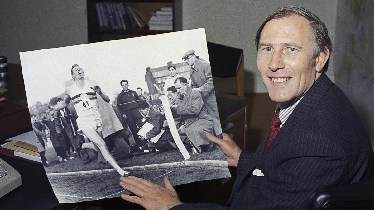 Roger Bannister, en una imagen de 1974, mostrando una foto de 20 años antes batiendo el récord de la milla.