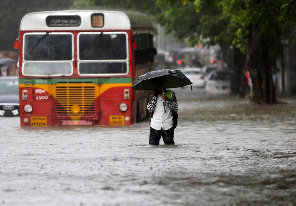 Un hombre pasa junto a un autobús varado en un camino inundado por las fuertes lluvias en Mumbai, India