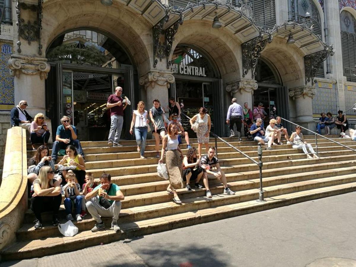 Turistas y usuarios sentados en la escalera del Mercat