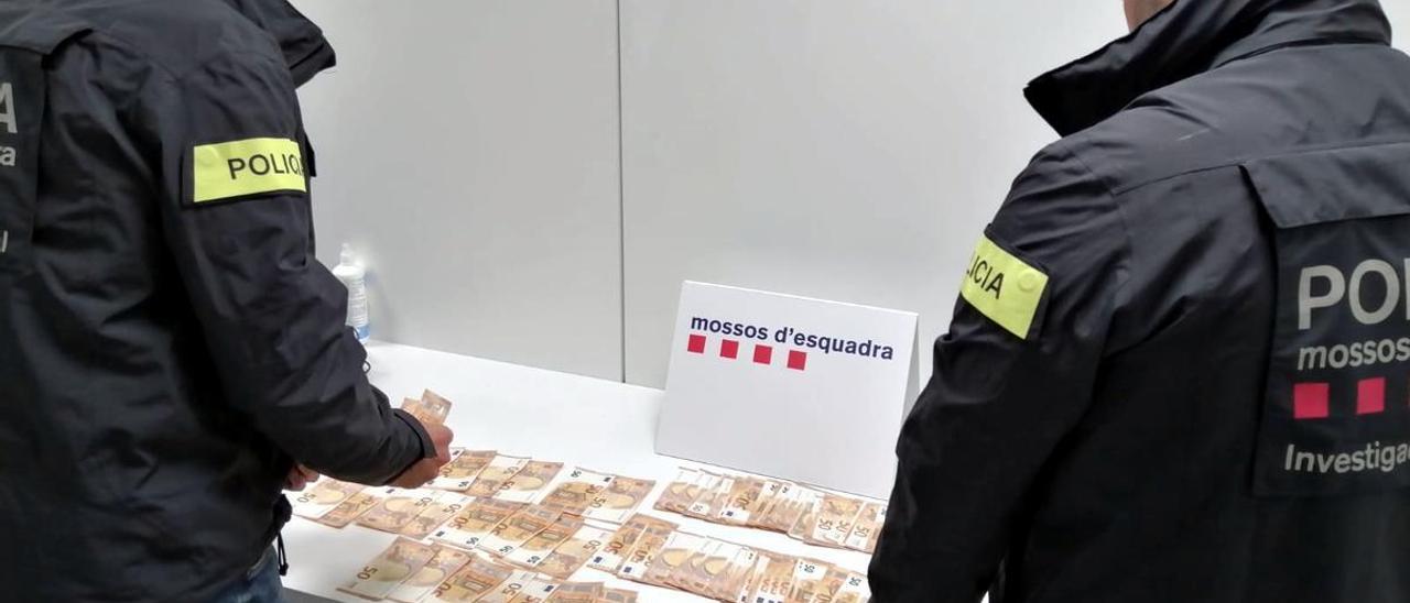 Dos agentes de los Mossos con parte del botín de la mujer detenida por estafar más de 74.000 euros con suplantación de identidad.