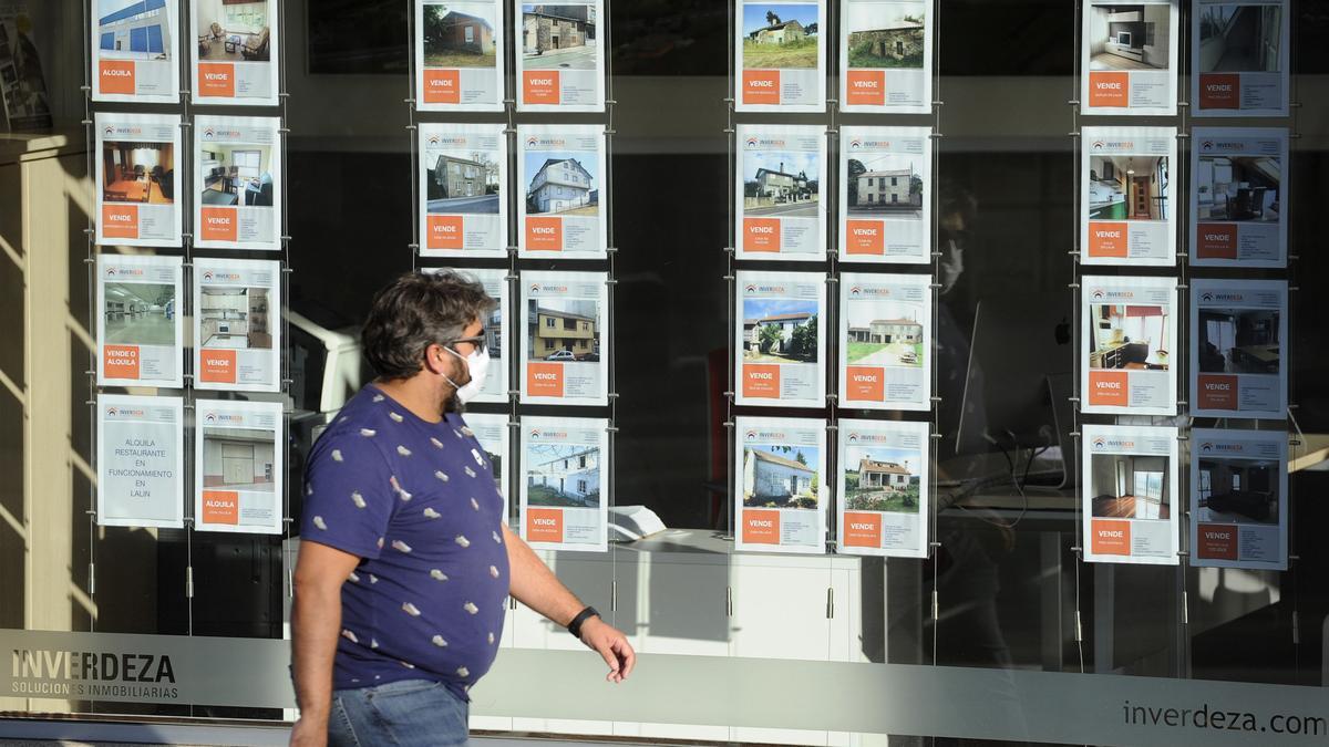 GENTE PASANDO DELANTE DE CARTELES DE VENTA DE INMUEBLES EN EL ESCAPARATE DE LA INMOBILIARIA INVERDEZA, EN LALIN.