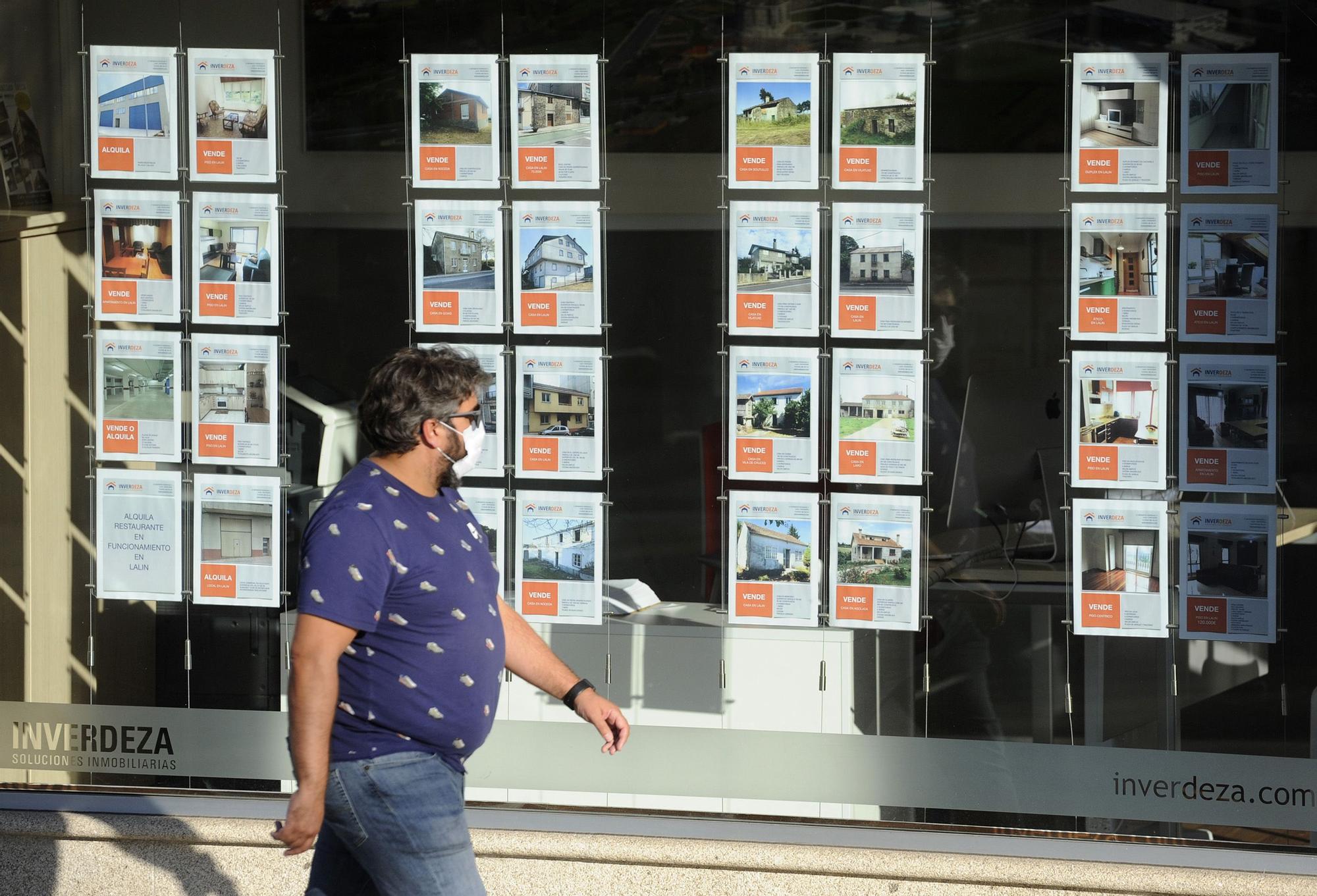 GENTE PASANDO DELANTE DE CARTELES DE VENTA DE INMUEBLES EN EL ESCAPARATE DE LA INMOBILIARIA INVERDEZA, EN LALIN.