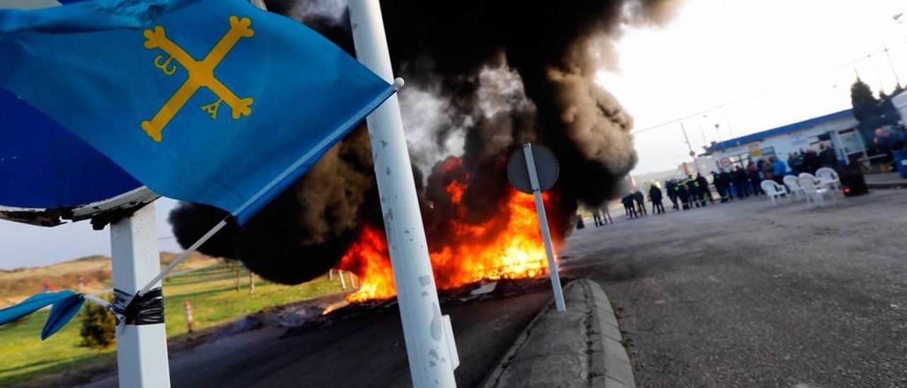 Una bandera de Asturias ondea a la entrada de la fábrica de aluminio de San Balandrán; en segundo término, una barricada en llamas y, al fondo, trabajadores concentrados en una pasada movilización.