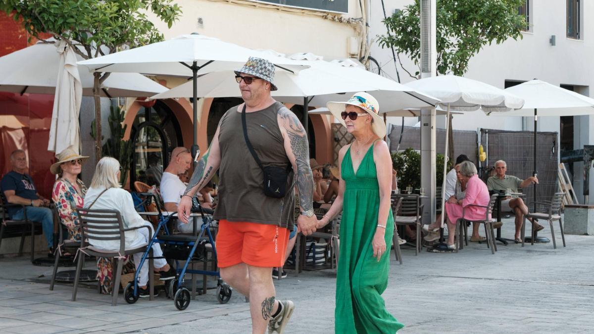 Una pareja de turistas pasean por el centro de Santa Eulària cogidos de la mano.