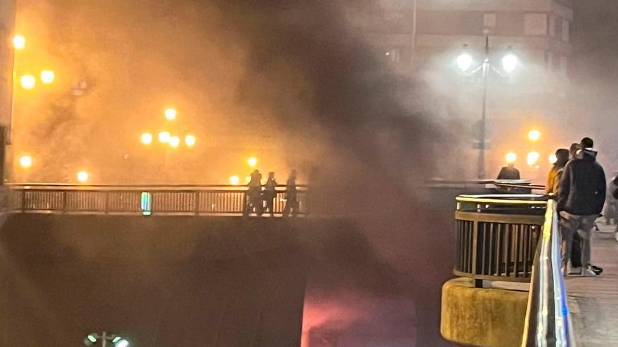 Los bomberos avanzan entre el humo sobre la zona incendiada, con las llamas asomando junto a las dependencias policiales de la Losa.