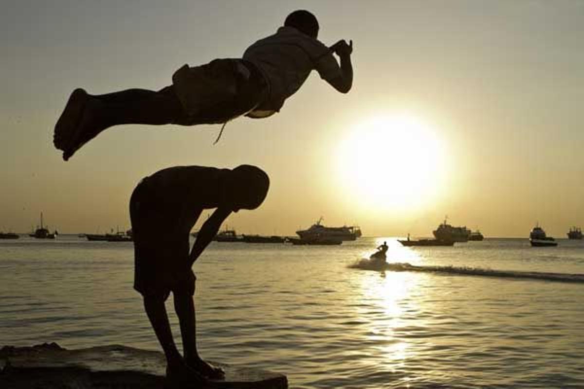Un niño salta sobre otro y hacia el mar en Stone Town.