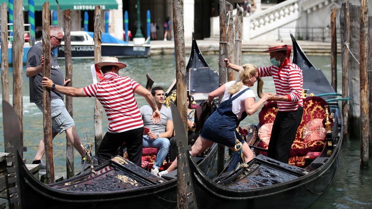 Dos gondoleros ayudan a unos turistas a subir a bordo, en Venecia.