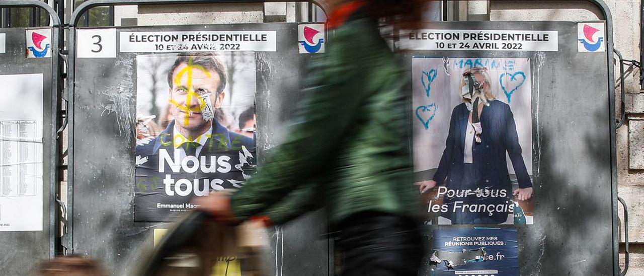 Una mujer pasa frente a los carteles electorales de Macron y Le Pen en una calle de París.