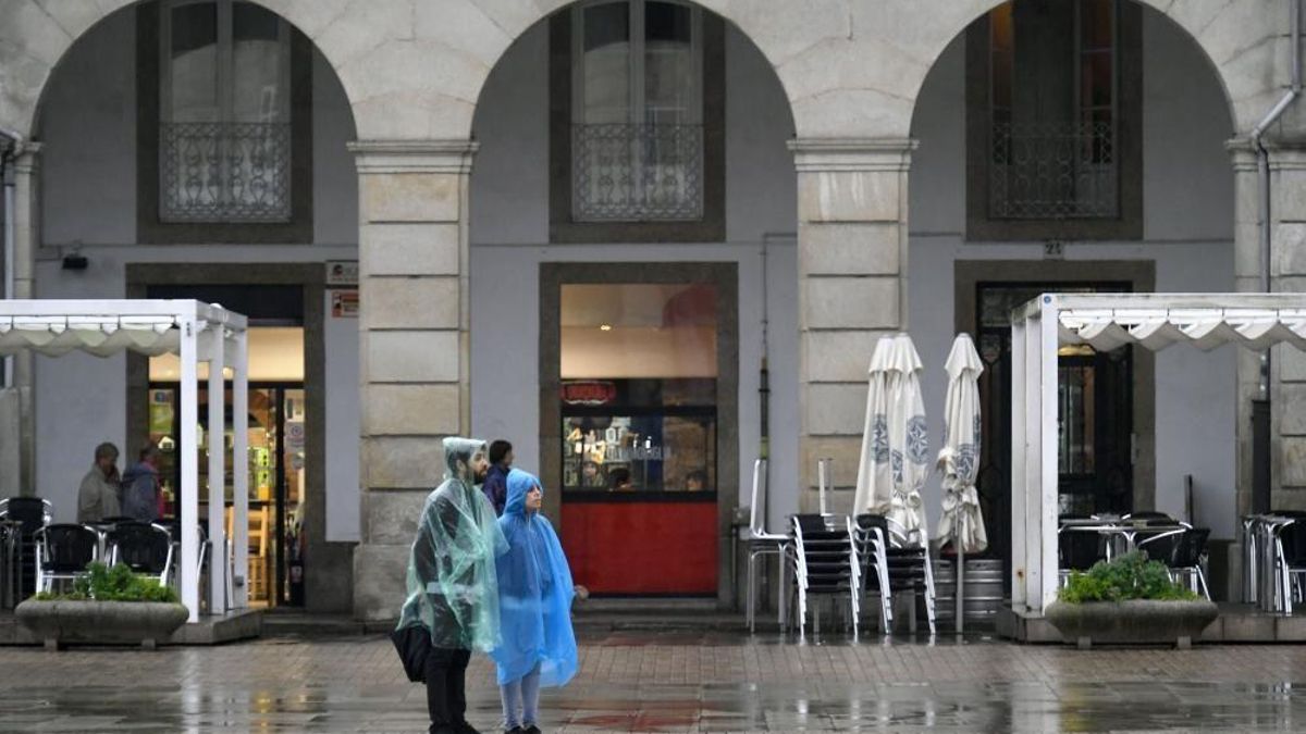Dos personas con chubasquero en la plaza de María de Pita un día con lluvia de verano.