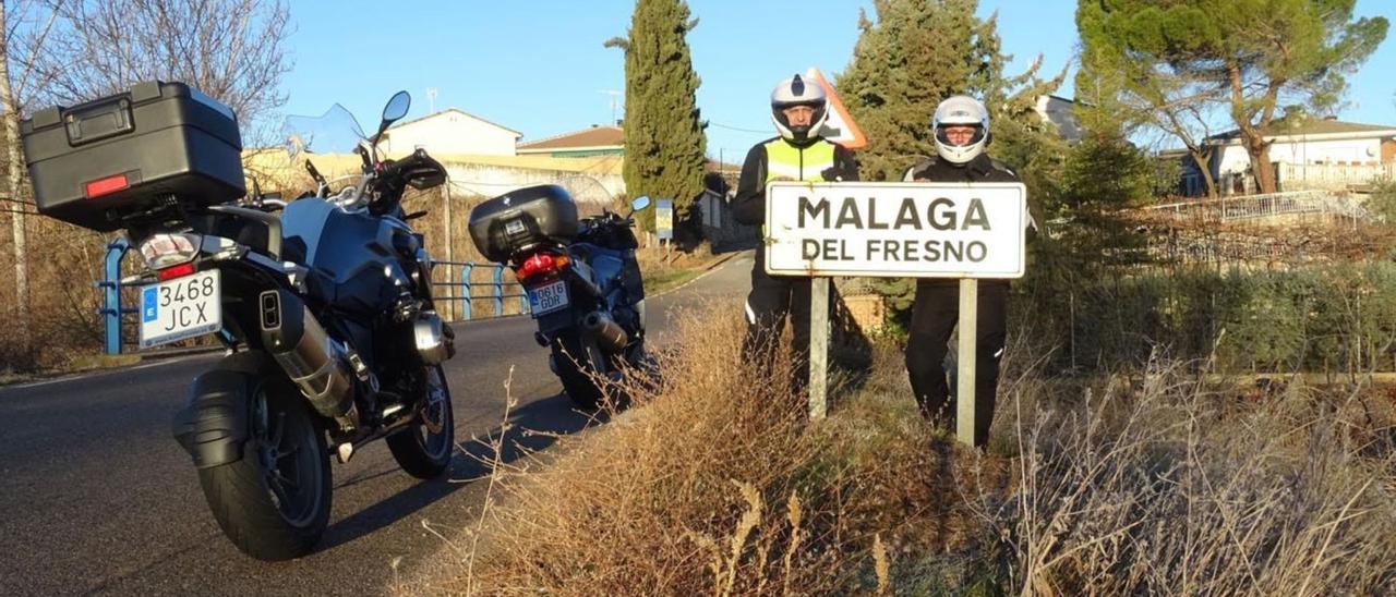 Dos moteros posan junto al cartel que indica la entrada al casco urbano de la manchega Málaga del Fresno.