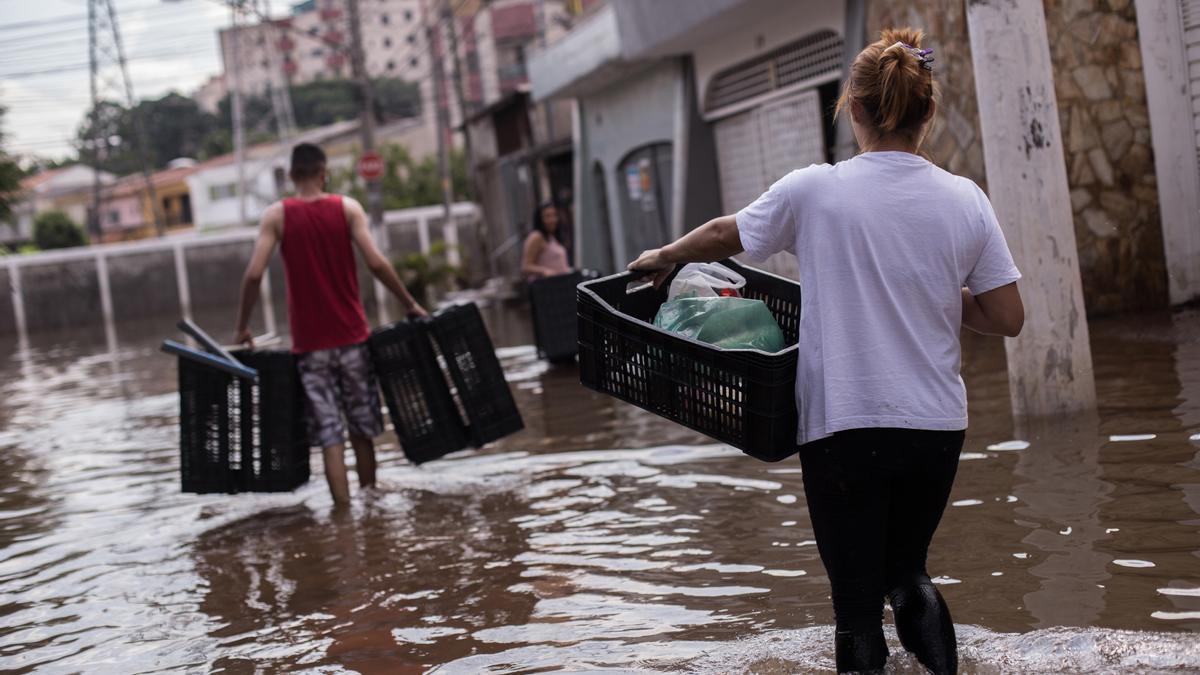 Varias personas vadean una calle inundada tras las inundaciones y corrimientos de tierra provocados por las fuertes lluvias.
