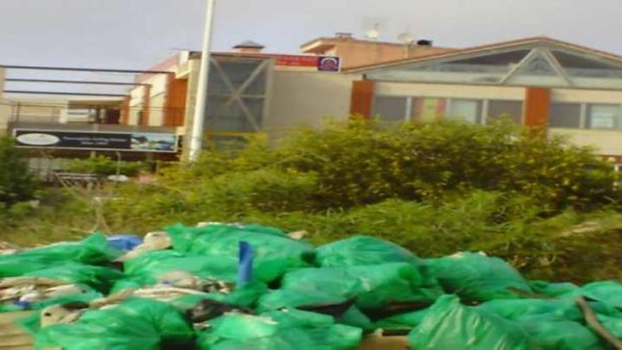 Bolsas de basura apiladas junto a un centro comercial.